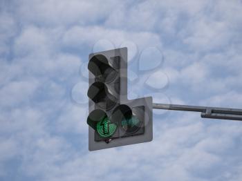 Green traffic light with an additional section against a cloudy sky.