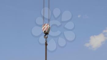 Crane hook with red and white stripes hanging, blue sky in background.