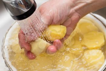 The cook washes the peeled potatoes in the water .