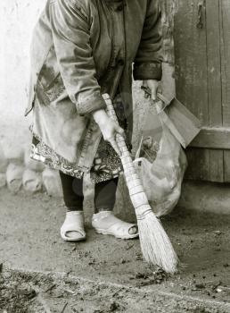 Woman sweeping the yard with a broom .