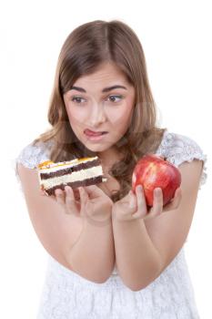 Young beautiful female choose from sweet cake and red apple, on white background