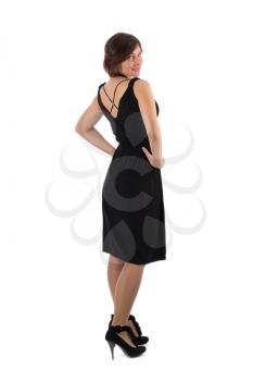 Lovely girl looks out from behind his back in the studio in a black dress. Isolate on white.