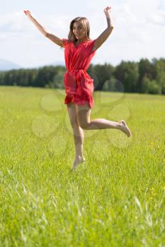 Young girl in a red dress jumping in a field on a sunny day.