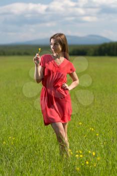 20 year-old girl in a red dress with a yellow flower in a field on a sunny day