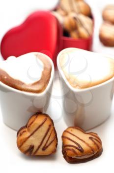 heart shaped cream cookies on red heart metal box and couple of cappuccino coffee cups