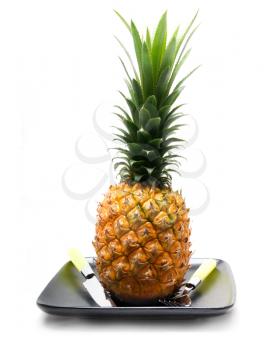ripe vivid pineapple on a black plate with knife and fork isolated over white
