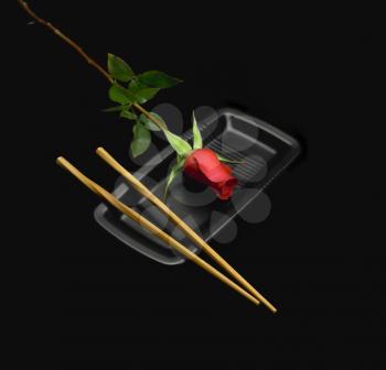 red rose on a japanese plate with chopstick over black background