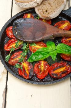 oven baked cherry tomatoes with basil and  thyme on a cast iron skillet and wood spoon
