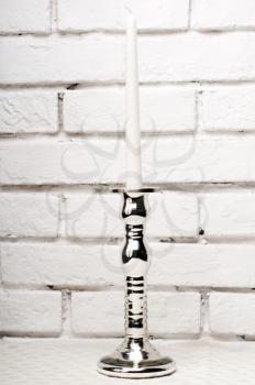 single silver candle holder over white brick wall background