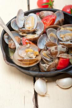 fresh clams stewed on an iron skillet over wite rustic wood table 