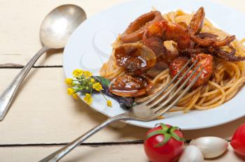 Italian seafood spaghetti pasta on red tomato sauce over white rustic wood table