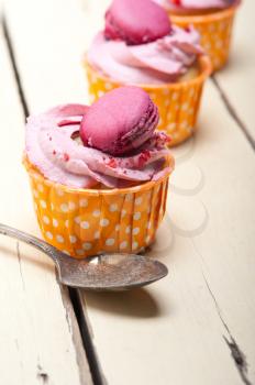 fresh pink berry cream cupcake with macaroon on top over rustic wood table