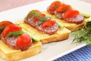 Sandwiches with salami, cheese, cherry tomato and dill on plate.