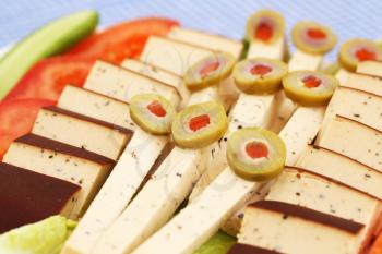 Cheese, olives and vegetables on plate.