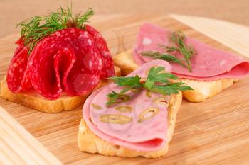 Sandwiches with salami and mortadella on wooden board.