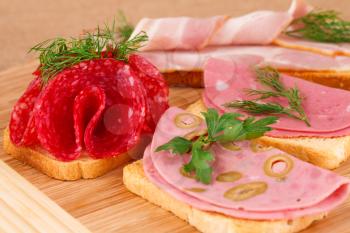 Sandwiches with salami, bacon and mortadella on wooden board.