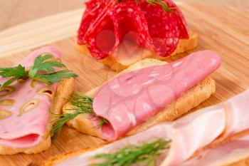 Sandwiches with salami, bacon and mortadella on wooden board.