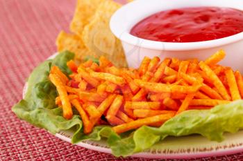 Potato chips,  red sauce and lettuce leaf isolated on colorful tablecloth.
