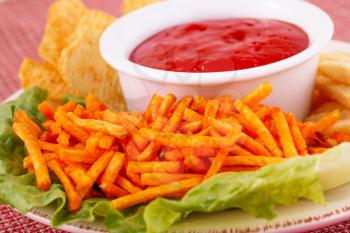 Potato chips,  red sauce and lettuce leaf on colorful tablecloth.