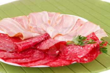 Salami and bacon on plate isolated on green background.