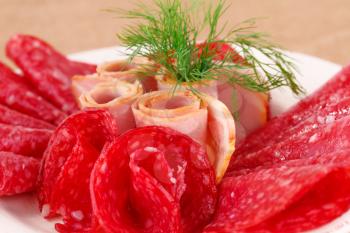 Salami and bacon on plate closeup image.