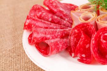 Salami and bacon on plate isolated on beige background.