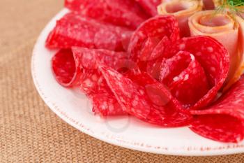 Salami and bacon on plate isolated on beige background.