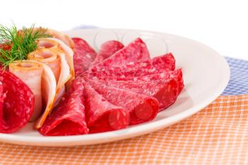 Salami and bacon on plate isolated on kitchen towels background.
