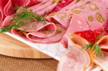 Salami, mortadella and bacon on plate on beige background.