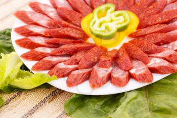 Fresh sausages, peppers in plate and green salad leaves on bamboo mat background.