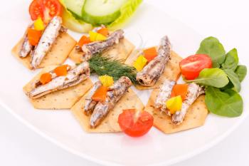 Fish and peppers on crackers with vegetables on white plate. 