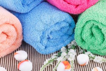 Colorful rolled towels with flowers and stones on cloth background.