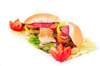 Sandwiches with fresh vegetables, salami and cheese on plate.