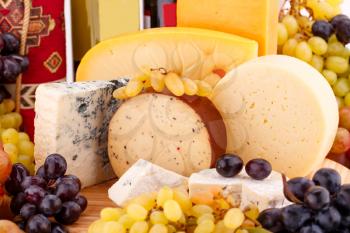 Various type of cheese, wines and grapes on wooden board closeup picture.