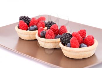 Fresh ripe berries in tartlets on brown plate.