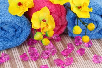 Colorful rolled towels, yellow orchid flowers and pink stones on cloth background.