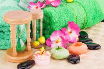 Spa set with towels, candles, sandglasses, stones and flowers on bamboo background.