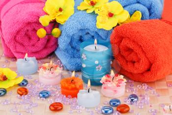 Spa set with towels, candles, stones and flowers on bamboo background.