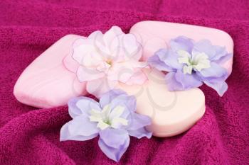 Colorful soaps and flowers on pink towel.