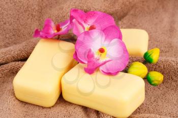 Yellow soaps and orchid flowers on brown towel.