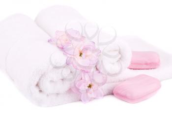 White rolled towels with soaps and flowers on white background.