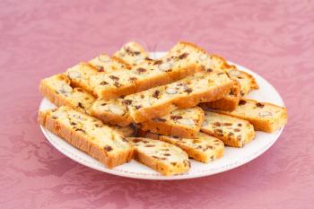 Crackers with nuts and raisins in plate on pink cloth background.
