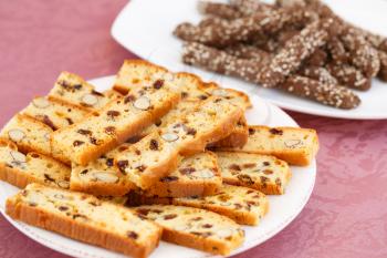 Carob crackers and crackers with nuts and raisins in plates on pink cloth background.