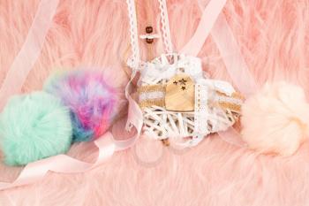 White wooden heart with ribbon and fluffy balls on pink fur background.