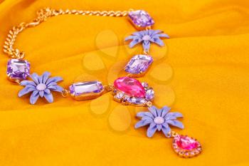 Stylish necklace with colorful stones on yellow fabric background.