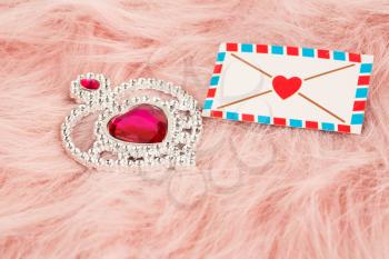 Jewelry heart with stones and envelope on pink fur background.