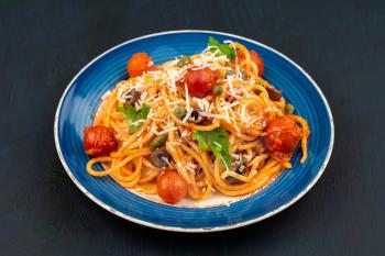 Pasta spaghetti Puttanesca on blue plate on dark wooden background. Italian cuisine.