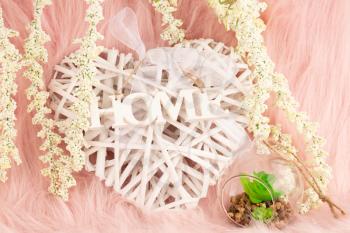 Home decoration on pink fur background. Wooden heart with ribbon and word home, white flowers and florarium closeup picture.