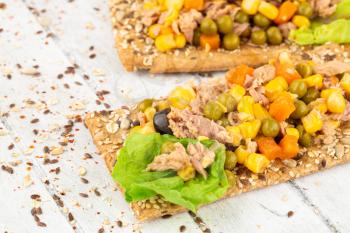 Sandwiches with crackers, tuna fish, corn and carrot on gray wooden background.