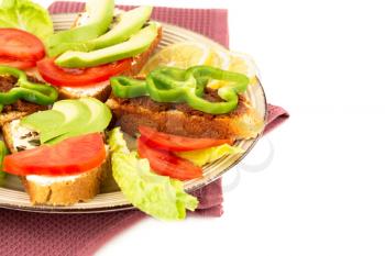 Sandwiches with cheese, sundried tomatoes, pepper, avocado and seeds, lettuce, lemon on beige  plate on towel on white background.